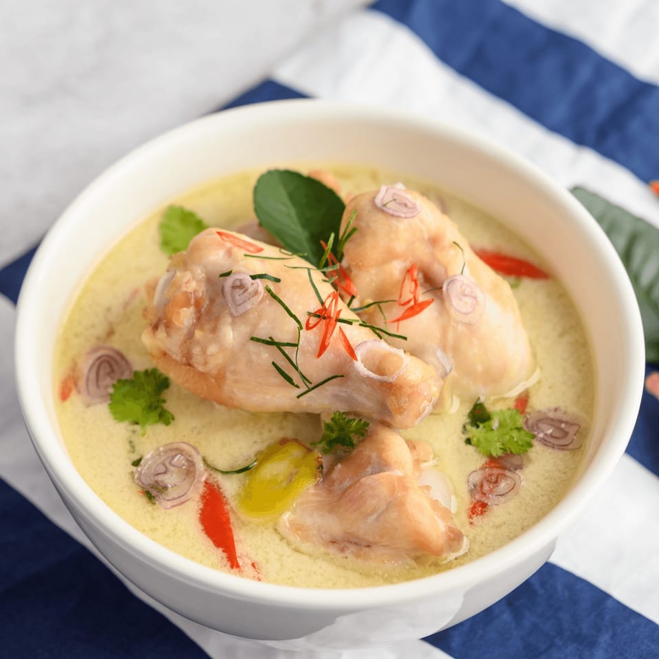 Chicken in a creamy yellow sauce, garnished with red chilies, herbs, and sliced shallots.
