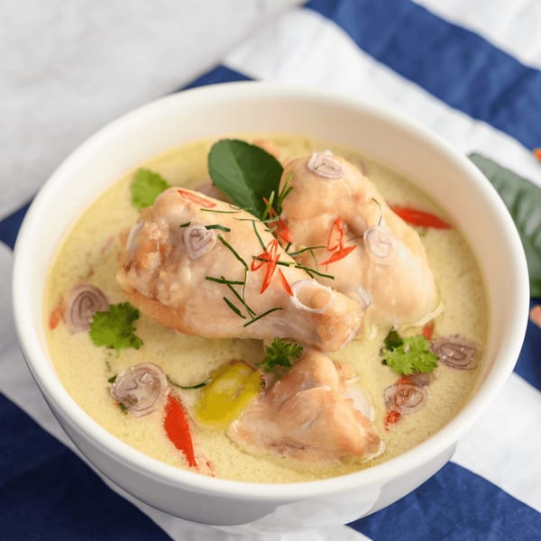 Chicken in a creamy green curry sauce, garnished with herbs, chilies, and shallots.