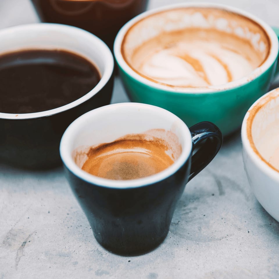 Several coffee cups, some full of dark coffee, others with espresso and latte art remnants.