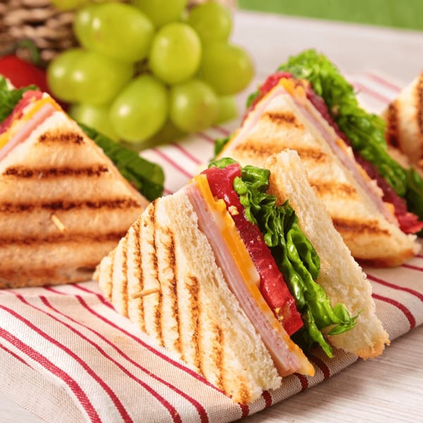 Grilled sandwiches with ham, cheese, lettuce, and tomato, served with green grapes.