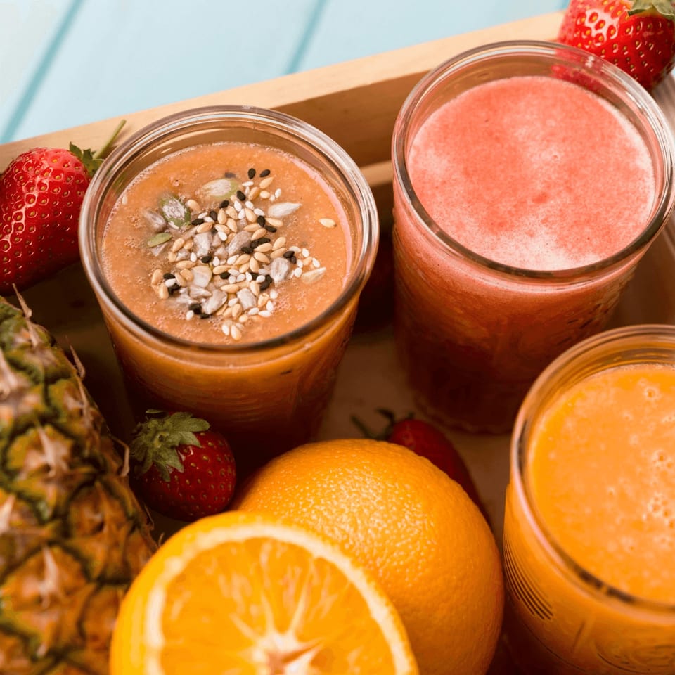 Three fresh fruit smoothies with strawberries, pineapple, and oranges in a wooden tray.
