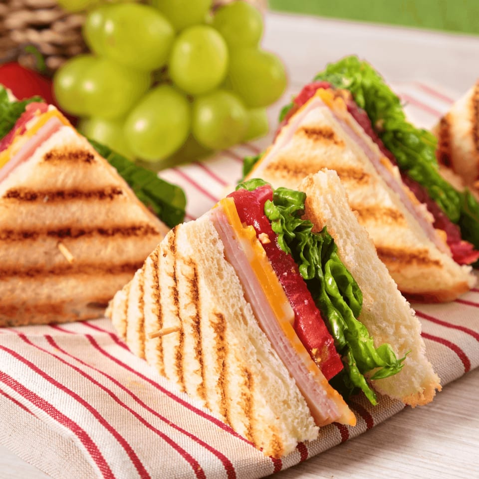Grilled sandwiches with ham, cheese, lettuce, and tomato, served with green grapes.